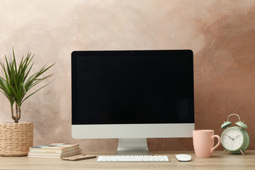 Workplace with computer, plant and alarm clock on wooden table. Light brown background
