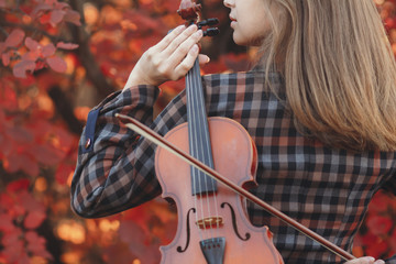 beautiful young woman playing violin on a background of red foliage, romantic girl in dress playing a musical instrument in nature, musical performance outdoors, concept of hobby and passion in art