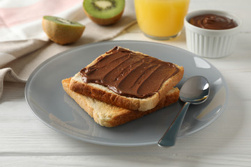 Toasts with choco cream on plate, kiwi and juice on wooden background, close up