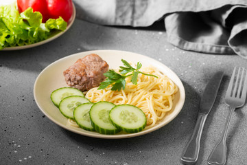 Pasta, cutlet and cucumbers on a beige plate on a gray table
