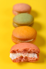 colorful macaroons and the front one with half eaten on yellow background