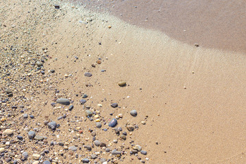 Background of wet sand with pebbles after the departure of the coastal wave