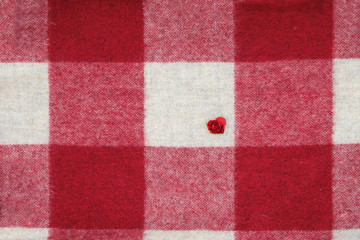 Plaid surface with a small artificial rose in a white square. Red and white squares.