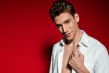 sexy young elegant man in unbuttoned shirt on red background