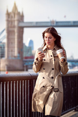 Fototapeta premium Frau im Trenchcoat Mantel mit Handy und Kaffee in der Hand vor der Skyline von London