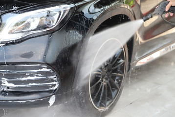 Closeup of black car cleaning, washing with  high pressure water spraying.