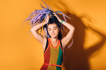 Hipster woman wearing in rasta dress and a rasta color make-up is dancing to reggae music. Orange background