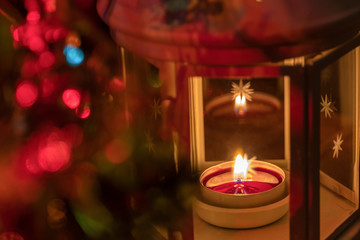 Festive Christmas candle in a lamp on a blurry colorful dark background with multi-colored lighting with bokeh. Focus with shallow depth of field.