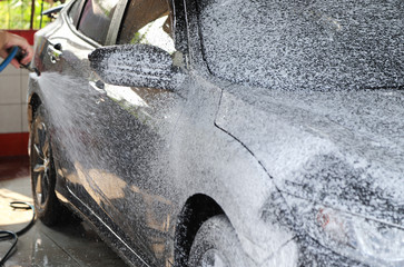 Closeup of black car cleaning, washing with  high pressure foam spraying.