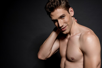 smiling sexy young naked man with muscular torso posing on black background