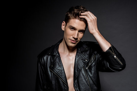 handsome sexy young man in biker jacket touching hair on black background