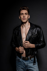 Fototapeta na wymiar sexy young man with muscular torso in biker jacket and jeans on black background