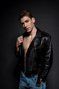 handsome sexy young man in biker jacket and jeans on black background