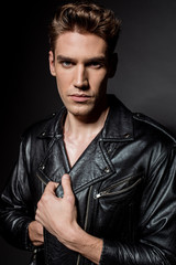 Obraz premium sexy young man in biker jacket looking at camera on black background