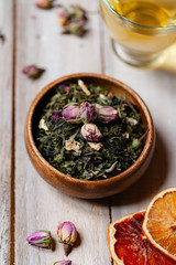 Obraz na płótnie Canvas Natural organic dry leaves of green tea with rose flowers and fruits in wooden bowl. Traditional source of relaxation and detention, atmosphere of spa. Healthy and delicious beverage