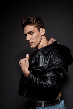 sexy young man with muscular torso in biker jacket looking at camera on black background
