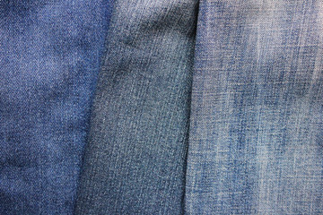 Naklejka premium Jeans background of blue denim clothing. Three pairs of various jeans, light and dark blue denim fabric textures, empty old trousers wallpaper 