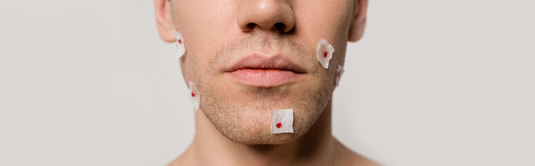 cropped view of naked man with bloody wounds after shaving on face isolated on grey, panoramic shot