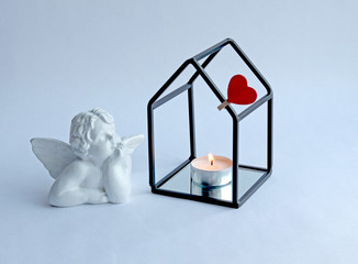 A white angel looks at a candle and a red heart