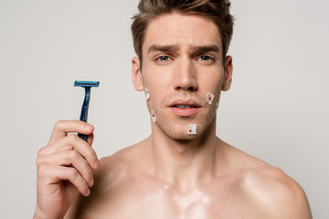 sexy man with muscular torso and bloody wounds after shaving holding shaver isolated on grey