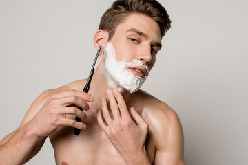 sexy man with muscular torso shaving with straight razor isolated on grey