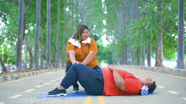Overweight woman helping her boyfriend doing sit-up exercise at the park. Shot in 4k resolution