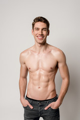 smiling sexy man with muscular torso with hands in pockets isolated on grey