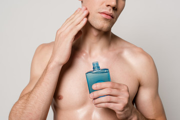 cropped view of sexy man with muscular torso applying after shave lotion isolated on grey
