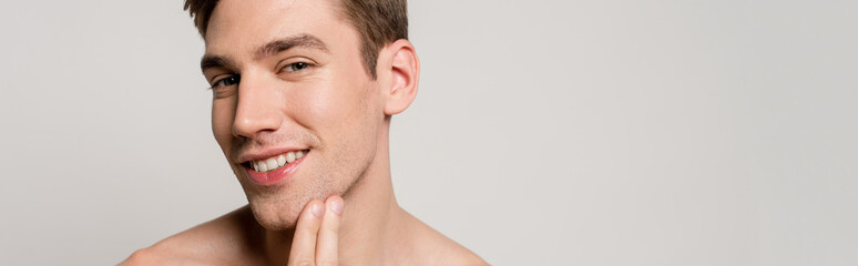 Obraz premium smiling naked sexy young man touching skin isolated on grey, panoramic shot