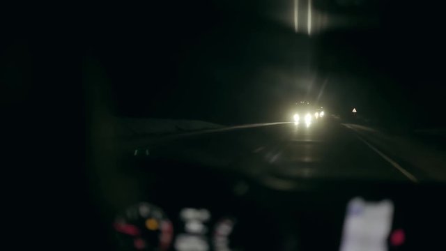 Video shot from inside the car. The driver drives cars at night in winter. The oncoming car shines headlights. Travelling by car. Road trip in the winter season. Slow mo