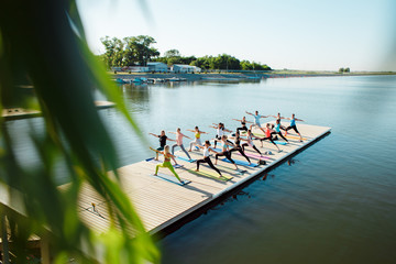 A big group of people attending yoga classes on a pontoon near the lake.