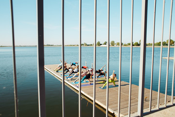 A big group of people attending yoga classes on a pontoon near the lake.