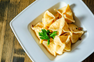 Meat dumplings - russian pelmeni, ravioli with meat on plate on a wooden background