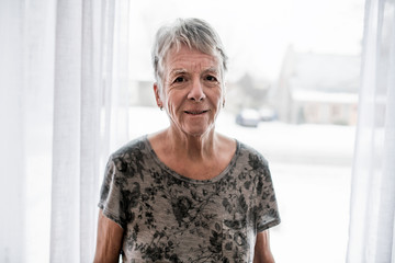 Sad senior woman at home close to window