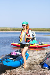 Obraz premium red-haired girl in red life vest standing near expedition kayaks