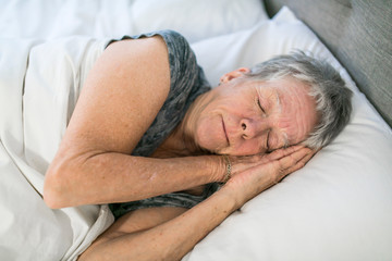 Senior aged woman on bed at home feeling sad