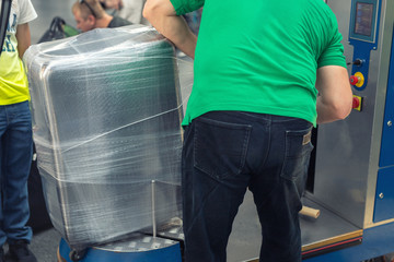 Worker wrapping suitcase with transparent protection film atairport deparure terminal before...
