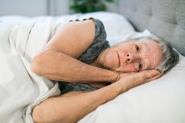 Senior aged woman on bed at home feeling sad