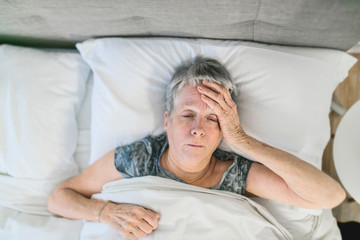 Senior aged woman on bed at home feeling sad