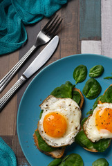 Fried eggs on a blue plate with green salad and bread for breakfast