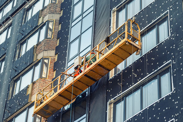 Suspended construction craddle near wall of hightower residentaial building with insulation and...