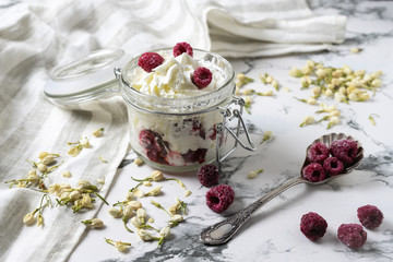 Whipped cream with fresh raspberries in a glass jar on a white marble background