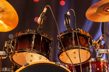 Drum set with bass drum, tom-toms, cymbals and microphones on the stage with yellow illumination