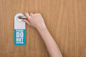 cropped view of woman holding door handle with please do no disturb sign