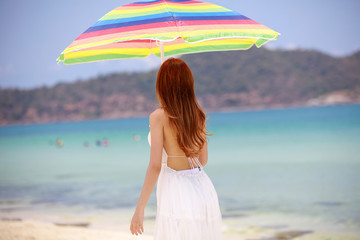 Young woman walk and hold colorful umbrella on whte beach