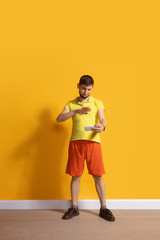 Fototapeta na wymiar Shocked, wondered. Young caucasian man using smartphone, serfing, chatting, betting. Full length portrait isolated on yellow background. Concept of modern technologies, millennials, social media.