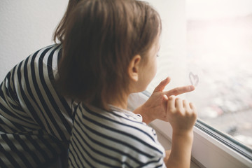 Little girl with her mother drawing heart on misted window glass