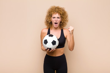 young afro woman shouting aggressively with annoyed, frustrated, angry look and tight fists,...