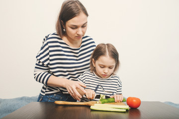 Obraz premium Young mother teaches her little daughter to cut vegetables