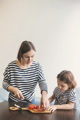 Young mother teaches her little daughter to cut vegetables